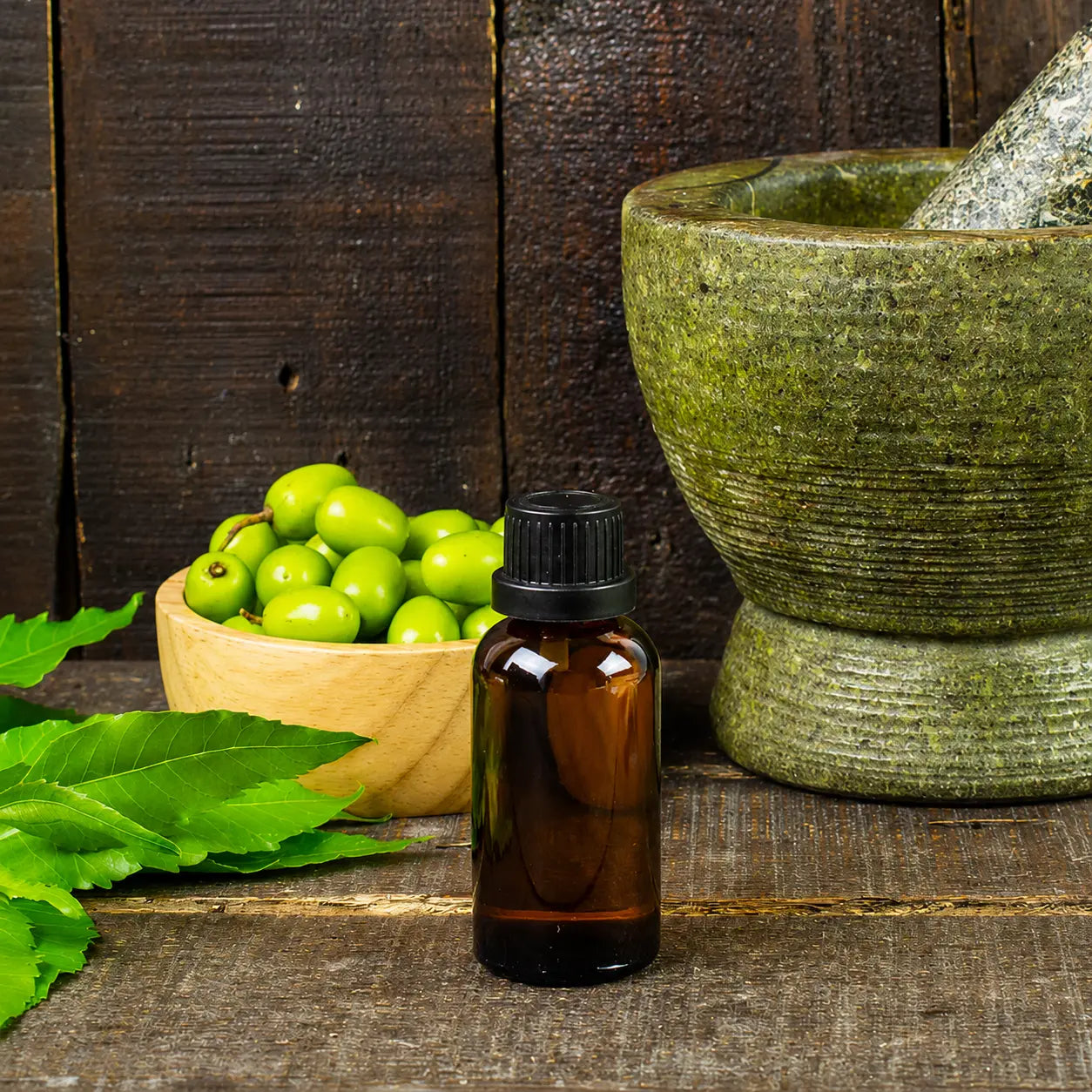 Amber bottle of neem essential oil with fresh neem leaves, neem fruits, and a traditional mortar and pestle on a rustic wooden surface