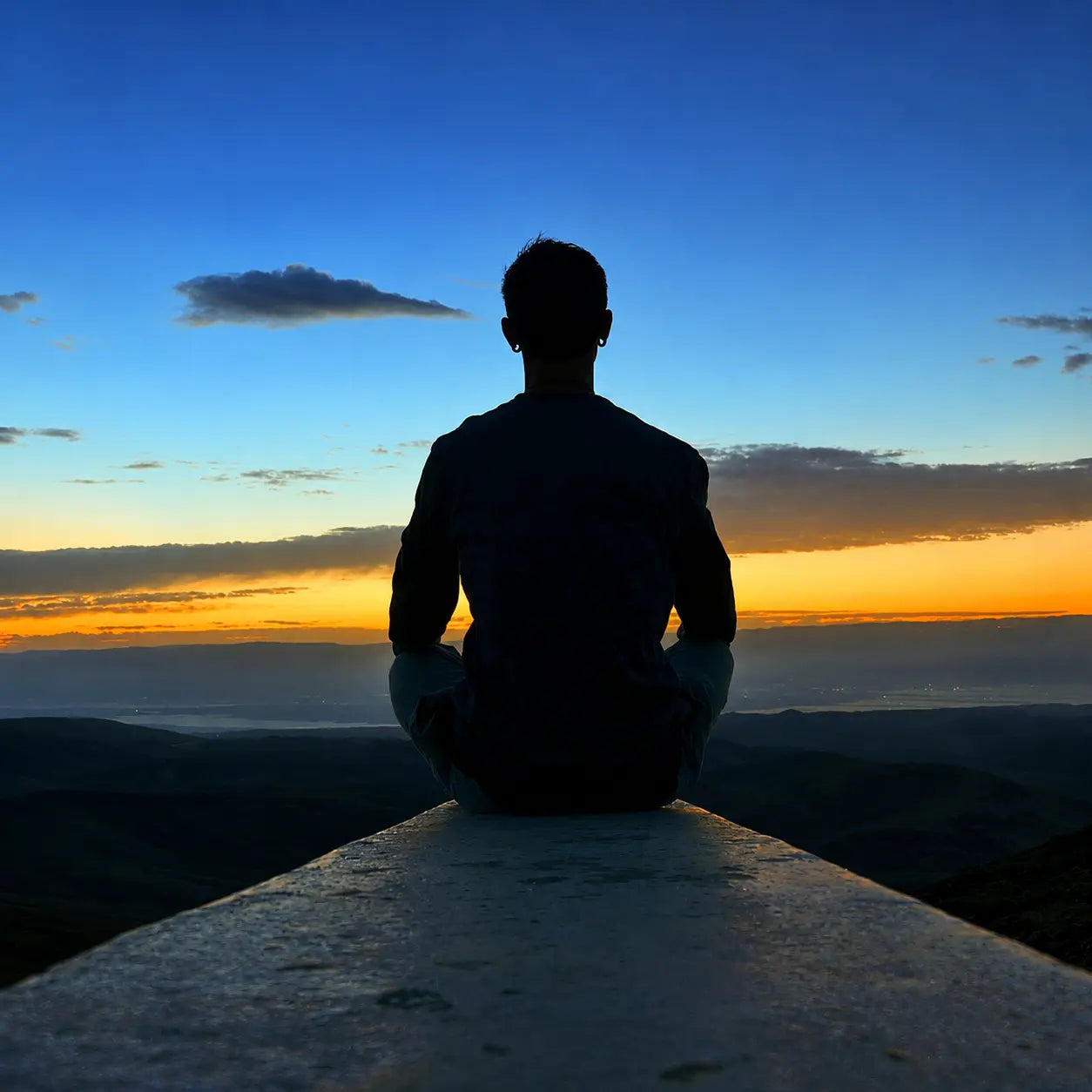 Person sitting peacefully on a viewpoint, watching a beautiful sunset over the mountains, symbolizing mindfulness and inner peace.