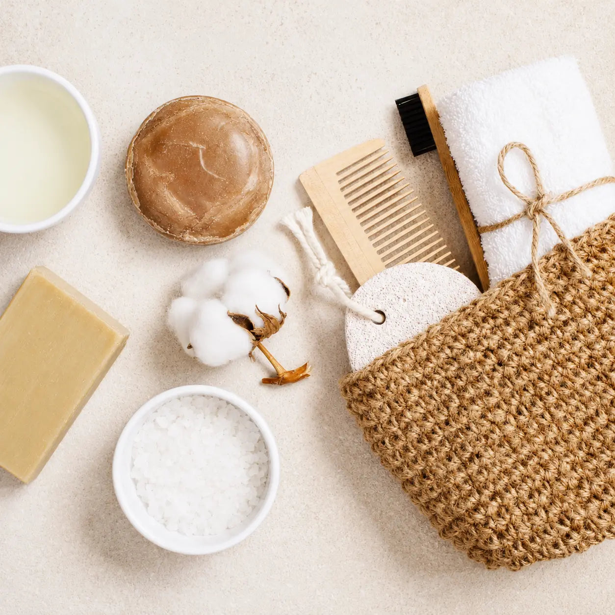 Flat lay of natural skincare essentials including handmade soap, bath salts, cotton, wooden comb, and eco-friendly spa accessories.